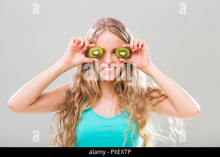 Beautiful young woman showing slices of kiwi on gray background. Stock Photo