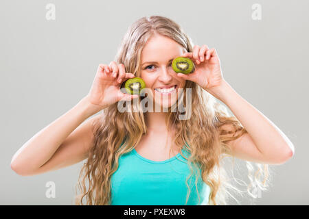 Beautiful young woman showing slices of kiwi on gray background. Stock Photo