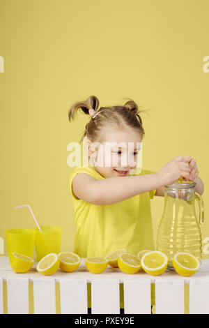 'When life gives you lemons make a lemonade' Five-year-old girl holding lemons making lemonade isolated on the yellow background. Stock Photo