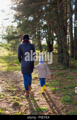 Mother holding her kid's hand while walking together in the forest Stock Photo