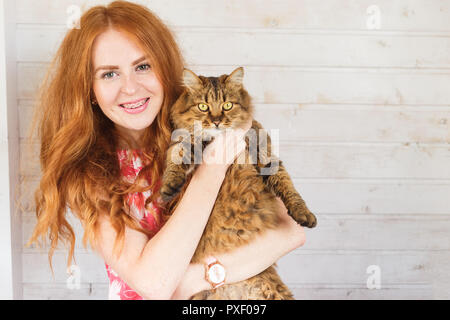 Young redhead woman with cat in arms. Stock Photo