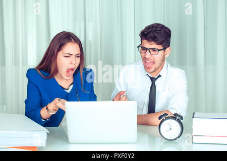 Stressed angry business woman and man with laptop looking at it sitting at table screaming at computer. Negative emotions in office life. Problems at  Stock Photo