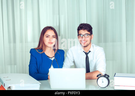 Couple in office behind laptop looking at you camera happy smiling. Business people freelance working at home. Positive face expression human emotion  Stock Photo