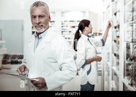 Bearded mature first-line pharmacist feeling joyful while working hard Stock Photo