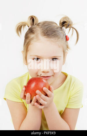 Cute five-year-old girl holding an apple close to her mouth isolated on the white background. Stock Photo