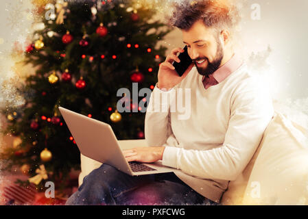 Busy freelancer speaking by phone and working on laptop before Christmas Stock Photo