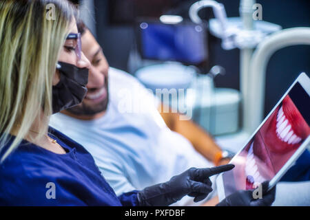 female dentist shows electronic device to male patient for smile design Stock Photo