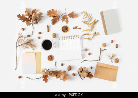 Autumn feminine workspace, desk with notepad, envelope, cup coffee, card and dry autumn leaves on white background, top view. Stylish office Stock Photo