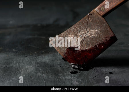 closeup of an old and rusty meat cleaver full of blood, stuck on a dark green rustic surface Stock Photo