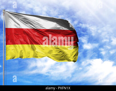 National flag of North Ossetia on a flagpole in front of blue sky. Stock Photo