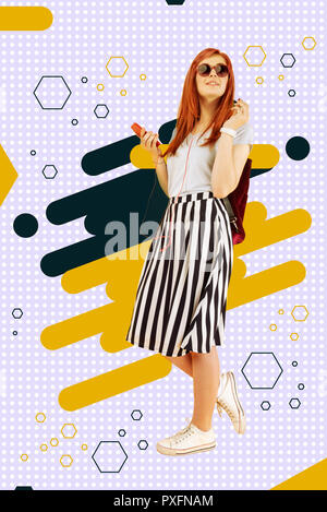 Stylish red-haired cheerful student listening to favorite song using her earphones Stock Photo
