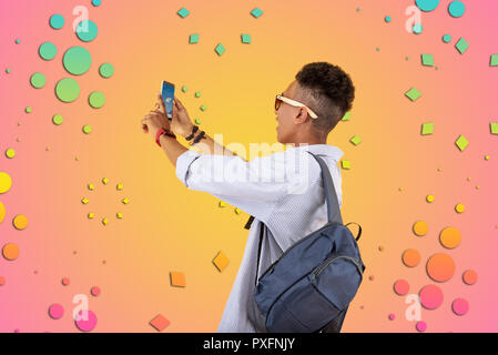 Mulatto teenager wearing blue backpack using his phone checking weather forecast Stock Photo