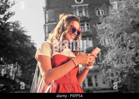 Curly woman wearing nice ring laughing while reading funny message on phone Stock Photo