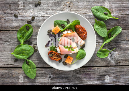 Cold snack or italian appetizer on plate - prosciutto with cheese. Table with food garnished dried tomatoes and basil leaves. Stock Photo