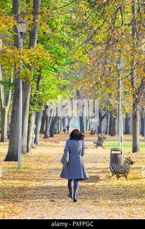 Girl with black hair walks in a beautiful park in autumn, with autumnal colored leaves, foliage and benches