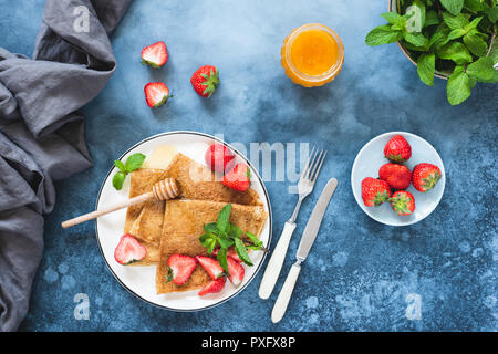 Crepes or blini with strawberries and honey on blue concrete backdrop, top with with copy space for text Stock Photo