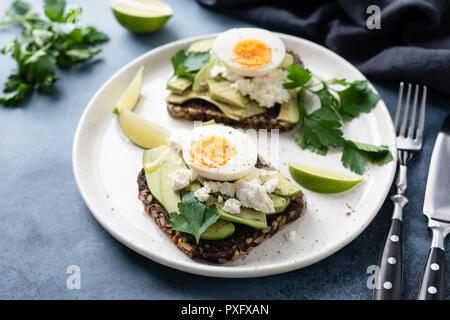 Healthy rye toast with avocado, egg, feta cheese on white plate. Healthy tasty breakfast, lunch or snack Stock Photo