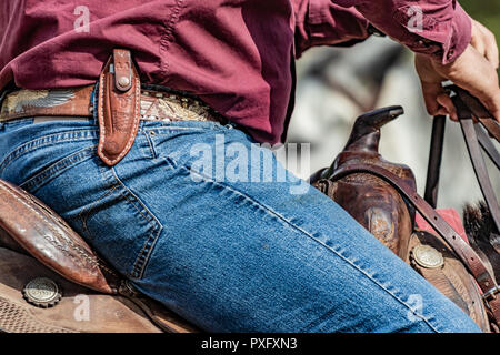 Horse rider with knife and blue jeans. Scenes from a rodeo and equestrian show, warming up phase, details of saddles, clothing, stirrups and brown hor Stock Photo