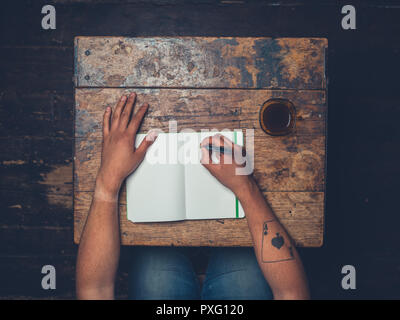 Overhead shot of man writing in notebook and drinking coffee Stock Photo