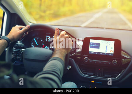 Male driver with hands on the steering wheel driving on road in autumn warm colors Stock Photo