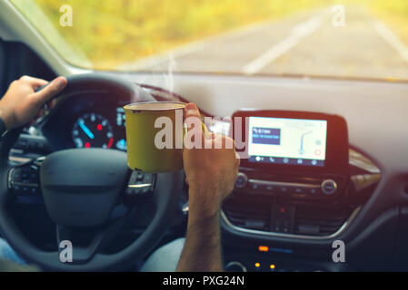 Male driver drinking hot coffee while driving on road in autumn warm colors Stock Photo