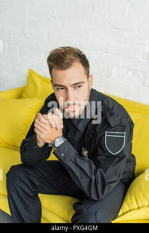 high angle view of thoughtful young policeman sitting on yellow couch in living room Stock Photo