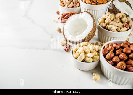 Various types of nuts - walnuts, pecans, peanuts, hazelnuts, coconut, almonds, cashews, in bowls, on a white marble table top view Stock Photo