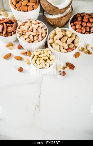Various types of nuts - walnuts, pecans, peanuts, hazelnuts, coconut, almonds, cashews, in bowls, on a white marble table top view Stock Photo