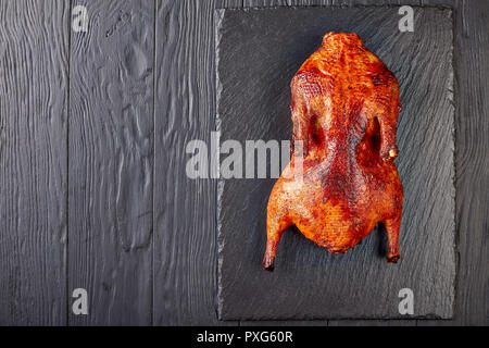 whole Amber-Hued grilled duck with extremely crispy skin on a black slate tray for Thanksgiving or Christmas Dinner, view from above, flatlay, copy sp Stock Photo