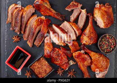 close-up of Juicy Peking Duck Carved Table-Side with extremely crispy flavour skin on a black slate tray with spices and sauce, view from above, flatl Stock Photo