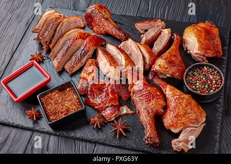 close-up of Juicy Peking Duck Carved Table-Side with extremely crispy flavour skin on a black slate tray with spices and sauce, view from above Stock Photo