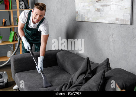 handsome young man in rubber gloves cleaning furniture and smiling at camera Stock Photo