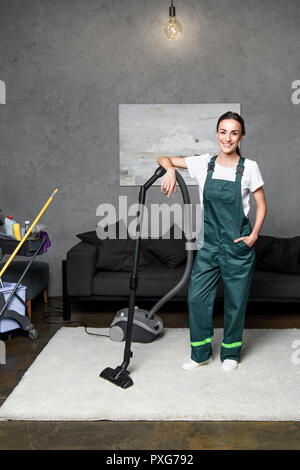 happy young female cleaning company worker leaning at vacuum cleaner and smiling at camera Stock Photo