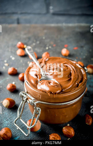 Breakfast confectionery and sweets concept. Homemade hazelnut chocolate spread in glass bowl with nuts, cocoa powder, dark blue concrete background. Stock Photo