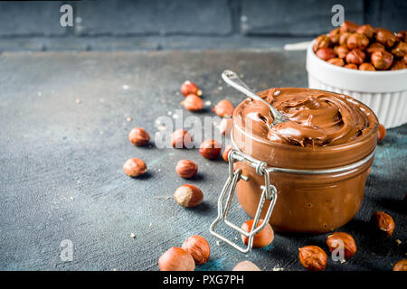 Breakfast confectionery and sweets concept. Homemade hazelnut chocolate spread in glass bowl with nuts, cocoa powder, dark blue concrete background. Stock Photo