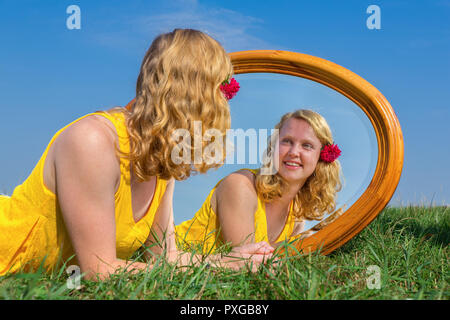 Young red-haired dutch woman lying in grass with mirror Stock Photo