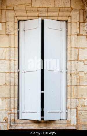 Old window with wooden white painted shutters on stone wall. The shutters are closed Stock Photo