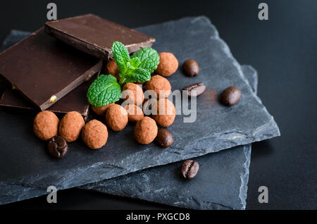 Heap of dark chocolate bars and coffee beans candy covered with chocolate with green mint leaves on dark slate board on black background. Selective fo Stock Photo