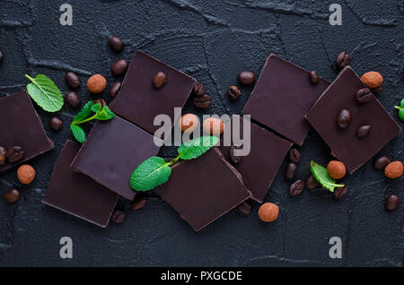 Dark chocolate with coffee beans candy covered with chocolate and green mint leaves on black background. Top view. Stock Photo