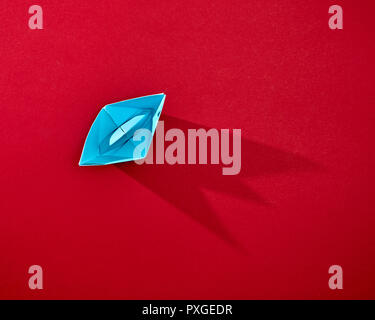 Handcraft paper blue ship isolated on red background with reflection of shadows and copy space. Top view Stock Photo