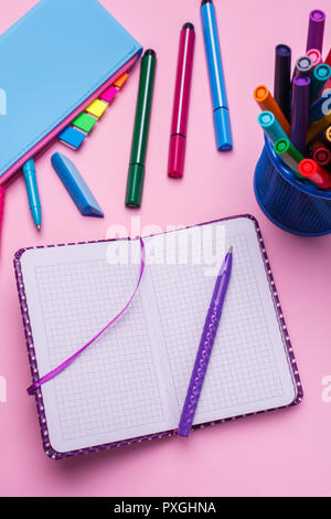 The pen is on an open notebook, next to a blue pencil case on a pink background Stock Photo