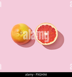 Two halves of a ripe grapefruit on a pink background with reflection of the shadow and space for text. Vitamin healthy food. Top view Stock Photo