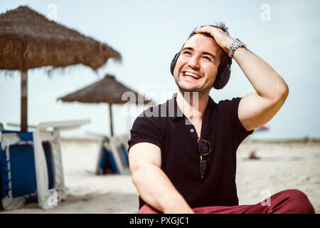 Fashionable man with fancy glasses and headphones sitting on the beach Stock Photo