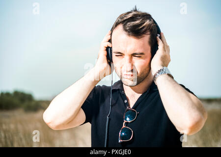 Young attractive man wearing black enjoying music on his headphones Stock Photo