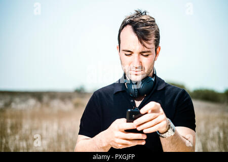 Fashionable young man with headphones setting playlist on smartphone Stock Photo