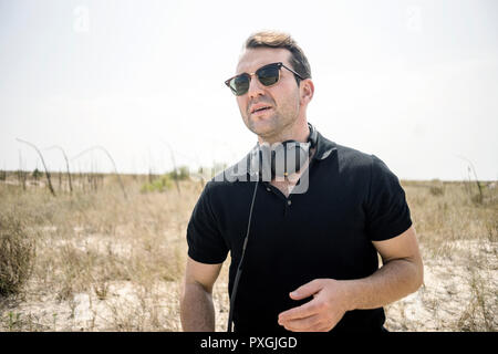Young man wearing fancy sunglasses and headphones on the desert Stock Photo