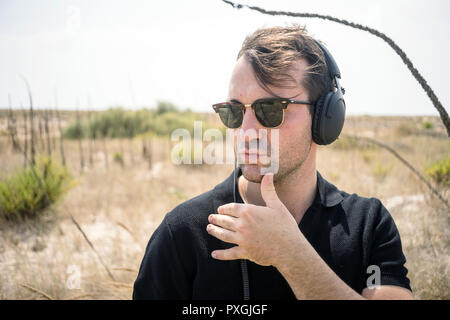 Fashionable man wearing fancy sunglasses and headphones in wilderness Stock Photo