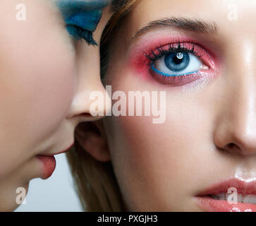 Two young women with blue and pink smoky eues makeup and glossy glitter skin. Closeup shot of blonde and brunette girls. Female friendship concept.