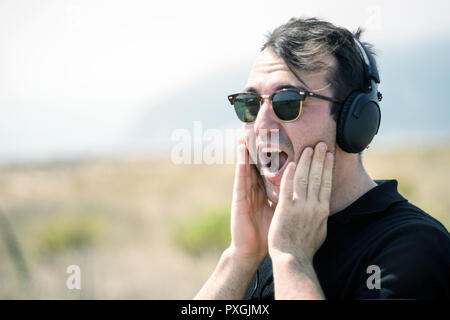 Surprised attractive man wearing sunglasses and headphones during sunny day Stock Photo