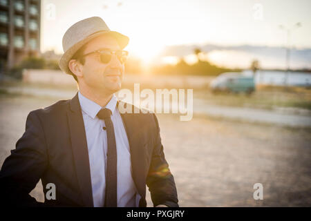 Lifestyle portrait of vintage looking young man in suit with sunglasses at sunset Stock Photo